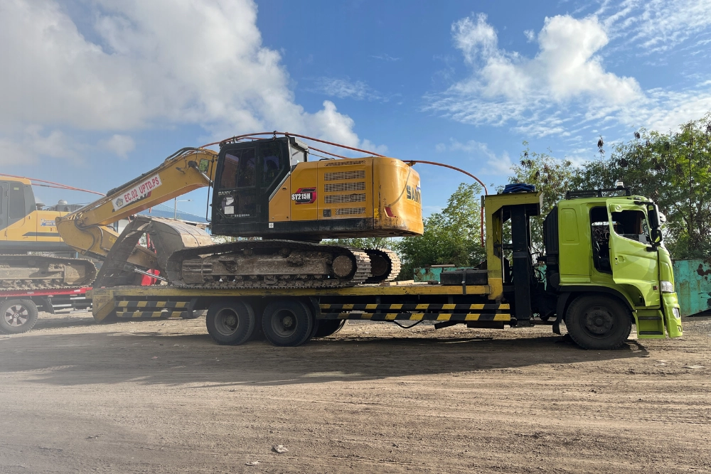 Flatbed trucking transporting heavy construction equipment on an open-deck trailer